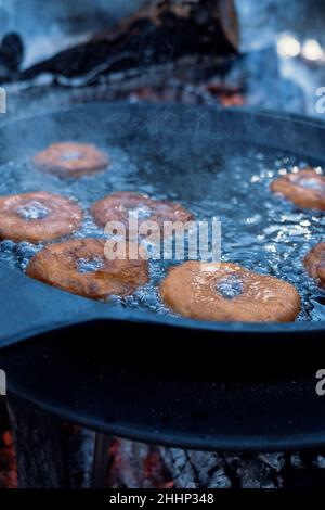 Hausgemachte Donuts Braten in Gusseisen Pfanne im Freien auf dem Campingplatz. Stockfoto