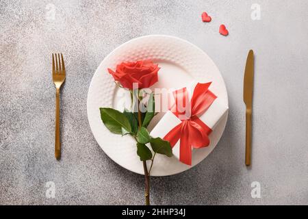 Romantisches Abendessen am Valentinstag mit rotem Geschenk und roter Rosenblume auf grauem Hintergrund. Draufsicht. Stockfoto