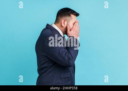 Portrait eines gutaussehenden Geschäftsmannes mit Gesichtsbart, der einen Anzug im offiziellen Stil trägt und die Augen schloss und nicht suchen möchte. Innenaufnahme des Studios isoliert auf blauem Hintergrund. Stockfoto