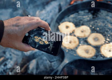Ein Foto von hausgemachten Donuts in gusseiserner Pfanne im Freien auf dem Campingplatz braten. Stockfoto