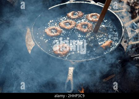 Hausgemachte Donuts Braten in Gusseisen Pfanne im Freien auf dem Campingplatz. Stockfoto