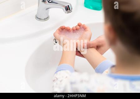 Seifenschaum in Herzform in den Kinderhände über dem Waschbecken und in den Händen der Mutter in einem hellen Badezimmer. Selektiver Fokus. Nahaufnahme Stockfoto