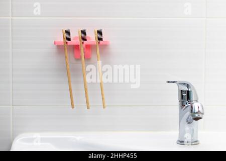 Drei natürliche Bambus-Zahnbürsten mit schwarzen Borsten in einem Halter vor einem gefliesten Hintergrund an der Badezimmerwand über dem Waschbecken. Selektiver Fokus. Stockfoto