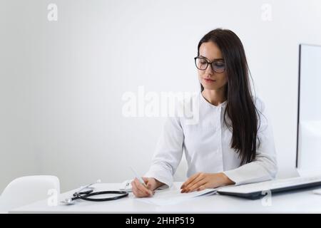 Porträt einer Ärztin, die am Schreibtisch sitzt und während der Arbeit im Büro etwas schreibt Stockfoto