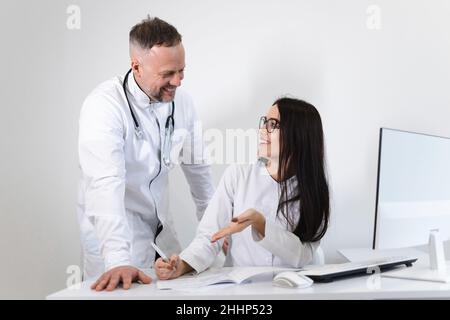 Die junge Ärztin berät sich mit dem Chefarzt. Zwei Kollegen von Ärzten haben Spaß beim Reden im Büro Stockfoto