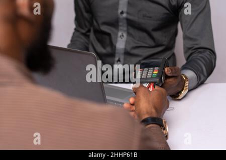 Afrikanischer Geschäftsmann, der ein POS-Gerät mit einem Kunden verwendet Stockfoto