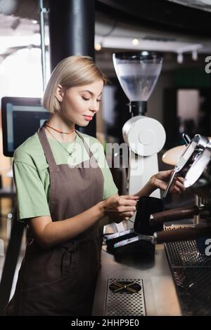 Junger Barista auf der Schürze mit Dampfdüse der Kaffeemaschine und Milchkännchen im Café Stockfoto