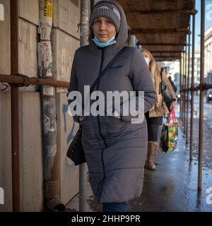 Belgrad, Serbien, 23. Januar 2022: Eine Frau mit Kapuze, die unter einem Gerüst über dem Bürgersteig die Straße entlang läuft Stockfoto