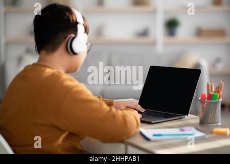 Junge, die zu Hause Headset und Laptop mit leerem Bildschirm verwenden Stockfoto