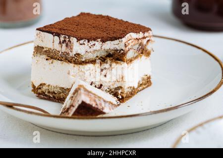 Tiramisu-Kuchen-Dessert mit Kaffee, Keks und Kakao als Zutaten auf einem hellen weißen Hintergrund serviert. Ein Stück Stockfoto