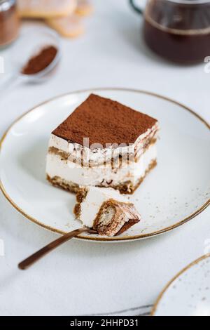 Tiramisu-Kuchen-Dessert mit Kaffee, Keks und Kakao als Zutaten auf einem hellen weißen Hintergrund serviert. Ein Stück Stockfoto