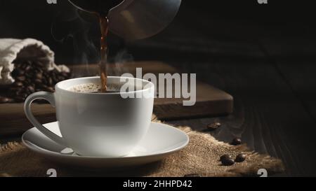 Gießen Sie frisch gebrühten heißen Cezve-Kaffee in eine weiße Tasse. Stockfoto