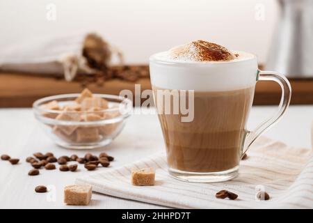 Latte-Kaffee, der in Schichten mit Schaum und einer knusprigen Schokoladenplatte auf einem hellen Küchentisch gegossen wird Stockfoto