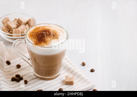 Latte-Kaffee, der in Schichten mit Schaum und einer knusprigen Schokoladenplatte auf einem hellen Küchentisch gegossen wird Stockfoto