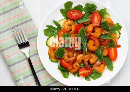 Frischer Salat aus Garnelen, Tomaten, Rucola und Kräutern auf einem weißen Teller, topview, Flatlay. Stockfoto