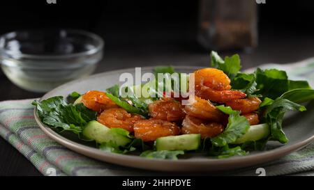 Frischer Salat mit gegrillten Garnelen, Gurken und Rucola, wunderschön auf einem Teller serviert. Stockfoto