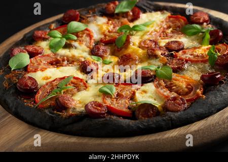 Schwarze Pizza mit Tomaten, Würstchen, Mozzarella und Basilikum. Teig mit gesundem Bambuskohlepulver. Stockfoto