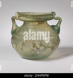Glas-Glas mit zwei Griffen 3rd–4th Jahrhundert n. Chr. römisch, palästinensisch lichtdurchlässig hellblaugrün; Griffe und Trails in gleicher Farbe. Abgerundeter, verbiegter Rand; unten hohler gefalteter Flansch; kurzer konkaver Hals; Hocken Sie den Kugelkörper; eingedrückter Boden mit innerem tritt und Pontitring in der Mitte; zwei Stabgriffe, die in großen Pads über die Spur zum Oberkörper aufgetragen werden, nach oben gezogen und herausgezogen, dann nach unten gefaltet und auf den Flansch eingeklappt, wieder aufgezogen, Und am oberen Rand des Randes abgeschnürt.eine Spur wird am Körper mit dem größten Durchmesser aufgetragen, um ein Zickzack-Muster zu bilden, das sich zwei Drittel um den Körper erstreckt; eine zweite Spur wird angewendet, um die zu vervollständigen Stockfoto