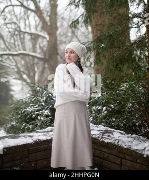 Warm gekleidete junge europäische Frau mit Zöpfen im Park mit Schnee Stockfoto