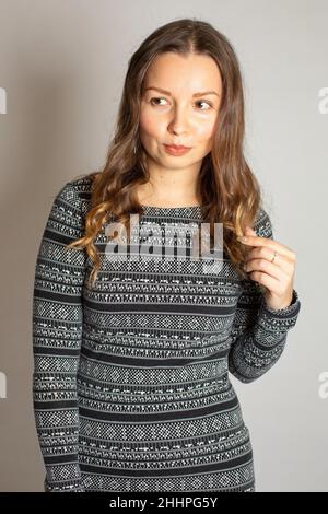Porträt einer jungen Frau in warmem gestreiftem Kleid, isoliert auf hellgrau stehend Stockfoto