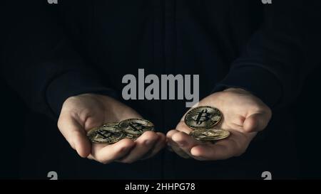 Eine Handvoll Bitcoins in männlicher Palmson mit dunklem Hintergrund. Finanzielle Einsparungen, Akkumulation im Kryptowährungskonzept. Selektiver Fokus. Stockfoto