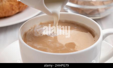 Milch oder Rahm aus nächster Nähe in frisch gebrühten Kaffee gießen Stockfoto
