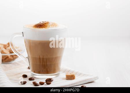 Latte-Kaffee, der in Schichten mit Schaum und einer knusprigen Schokoladenplatte auf einem hellen Küchentisch gegossen wird, Platz zum Kopieren. Stockfoto