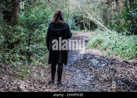 Moody geheimnisvolles Bild einer Frau, die durch einen schlammigen Pfad in einem leeren Wald geht, aufgenommen im Scadbury Park Nature Reserve, 11.. Februar 2018 Stockfoto