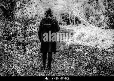 Moody geheimnisvolles Bild einer Frau, die in einem S/W-Ton durch einen schlammigen Pfad in einem leeren Wald geht, aufgenommen im Scadbury Park, 11.. Februar 2018 Stockfoto