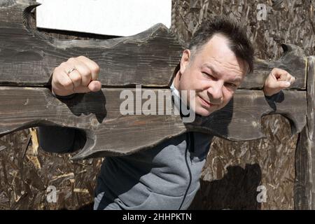 Porträt eines unglücklichen Mannes im Holzpranger im Freien Stockfoto