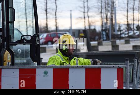 Ein Straßenarbeiter mit einem harten Hut steht in einem riesigen Loch, das in der Straße gegraben wurde, während er und sein Team Versorgungsleitungen unter der Straßenoberfläche reparieren Stockfoto
