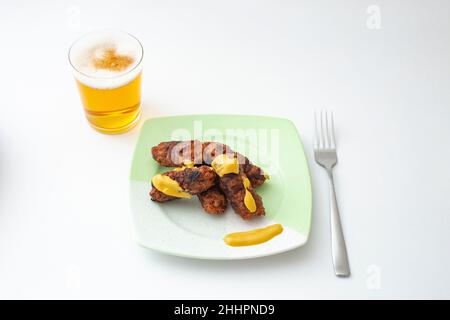 Rumänische, traditionelle Fleischbrötchen, genannt „mici“ oder „mititei“ mit Senf und einem Glas Bier, auf einem Teller, isoliert auf Weiß Stockfoto