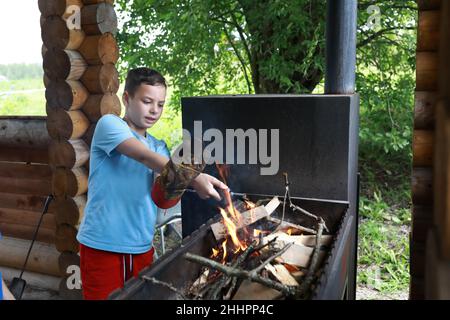 Junge zündet Feuerholz auf dem Grill im Pavillon, Karelia Stockfoto