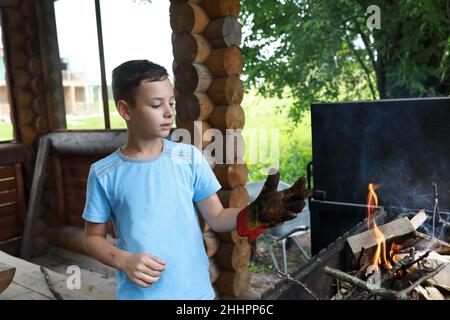 Kind zündet Feuerholz auf dem Grill im Pavillon, Karelia Stockfoto