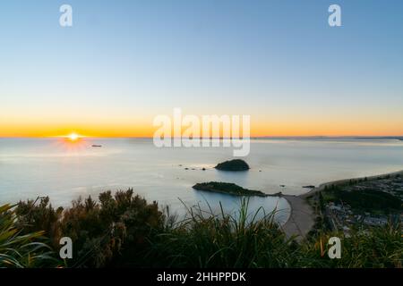 Vom Gipfel des Mount Maunganui aus geht die Sonne auf und erleuchtet das Meer. Stockfoto