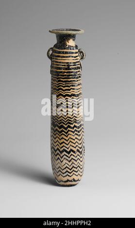 Glas-Alabastron (Parfümflasche) 5th. Jahrhundert v. Chr. Griechisch, östliches Mittelmeer Durchscheinend dunkelviolett, schwarz, mit Griffen in gleicher Farbe; Trails in opak-weiß und opak-türkisblau.Breite, leicht unebene horizontale Randscheibe; zylindrischer Hals mit nach unten verjüngender Kegel; gerundete Schulter; gerader zylindrischer Körper mit nach oben verjüngender Kegel und unten verwinkelt; Zwei vertikale Ringgriffe mit Schwänzen, die über der Traildekoration angebracht sind.Türkisblaue Spur am Rand der Randscheibe befestigt; eine weiße Spur wird auf den Hals aufgetragen, in einer Spirale um den oberen Teil des Körpers gewickelt und dann zu einer Irregula umwickelt Stockfoto