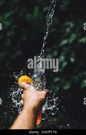 Vertikale Aufnahme einer Flasche, die mit herunterfallendem frischem Wasser aus dem Bach gefüllt wurde Stockfoto