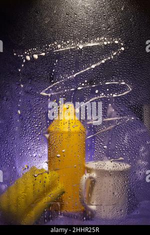 Auf einem dunklen, fliederfarbenen Hintergrund. Nahaufnahme von Haushaltsreinigungsprodukten und Küchenzubehör. Blick durch schmutziges Glas. Hochwertige Fotos Stockfoto