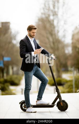 Schöner junger Geschäftsmann mit Handy auf Elektroroller Stockfoto