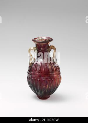 Glasamphoriskos (Parfümflasche) 1st. Jahrhundert n. Chr. römisch Durchscheinend rötlich-violett; Griffe aus farblosen Glas mit rauchig-grünem Farbton.Röhrenrand, ausgeklappt, über und in, und abgeflacht in einen auffackelnden Mund; hoher zylindrischer Hals; eiförmiger Körper; niedriger zylindrischer Boden, mit flachem, aber unebenem Boden; Zwei kleine Stangengriffe, die in einer Klauenauflage an der Oberseite des Körpers befestigt sind, aufgezogen, rund und innen, und auf den mittleren Teil des Halses gedrückt. Eine markante durchgehende Schimmelnaht am Hals, um den Körper herum und über den Boden.am Körper Fries aus 22 weit auseinander liegenden, abgerundeten Rippen am Oberkörper (zwölf auf einer Seite, Stockfoto