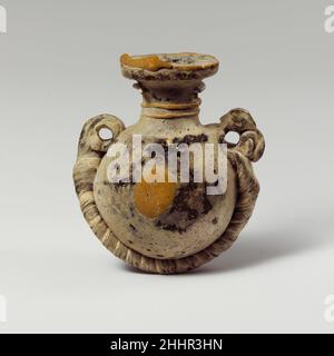 Glaslentoid Aryballos (Parfümflasche) 4th–3rd Jahrhundert v. Chr. Griechisch Halbdeckend gelbgrün, mit Griffen und Kordel der gleichen Farbe; Spuren und Blobs in opakes Gelb und Spur auf Kordel in opakes Weiß.breite flache Randscheibe mit strahlenden Werkzeugmarkierungen auf der Oberseite; zylindrischer Hals; fast horizontale Schulter; kugelförmiger lentoider Körper; konvexer Boden; Zwei große vertikale Ringgriffe, die an der Schulter über der Schnur befestigt sind.Eine Spur, die ungleichmäßig am Rand der Randscheibe befestigt und teilweise über dem Rand hervorragt; eine weitere unmarverierte, feine Spur, die sich in einer Spirale zweimal um den Hals gewickelt hat; ein ovaler marverierter Fleck wurde auf beide aufgetragen Stockfoto
