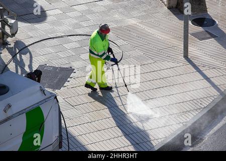 Arbeiter, die an sonnigen Tagen einen Bürgersteig mit einer Hochdruckwasserstrahlmaschine reinigen Stockfoto