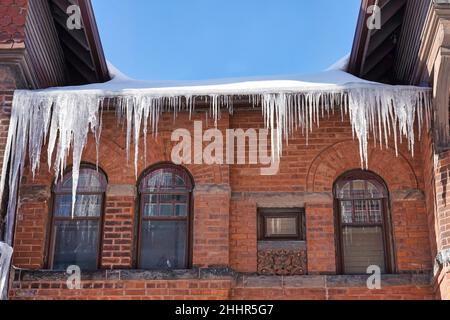 Altes Ziegelhaus mit großen Eiszapfen, die vom Dach hängen Stockfoto