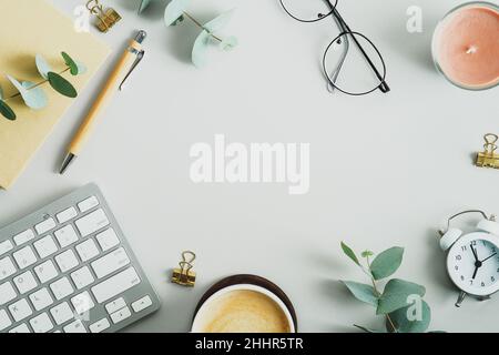 Draufsicht, flache Tastatur, Tasse Kaffee, Notizbuch aus Papier, Eukalyptuszweige auf dem Büroschreibtisch. Eleganter, femininer Arbeitsplatz. Stockfoto