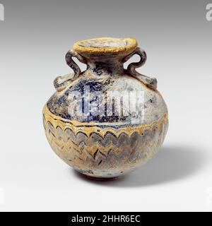 Glas Aryballos (Parfümflasche) Ende 6th–5th Jahrhundert v. Chr. Griechisch, östliches Mittelmeer Durchscheinendes Blau, mit gleichen farbigen Griffen; Spuren in opakes Gelb, mit einem anderen wahrscheinlich in opakes Türkisblau. Breite nach innen geneigte Randscheibe mit vertikal überstehender Lippe zu Mund; kurzer zylindrischer Hals; unregelmäßiger, fast kugelförmiger Körper; konvex, Leicht überstehende Unterseite; zwei Gurtgriffe in langen, abgeflachten Pads auf die Oberseite des Körpers aufgetragen, nach oben gezogen und nach außen, dann nach innen gewellt und an der Unterseite der Randscheibe befestigt.Gelbe Spur auf den äußeren Rand der Randscheibe aufgetragen; eine weitere breite gelbe Spur auf der Uppe aufgetragen Stockfoto
