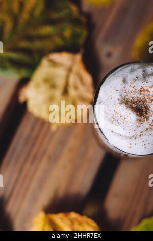 Ein Glas Kakao, gekrönt mit Schlagsahne und Zimt, umgeben von Herbstblättern Stockfoto