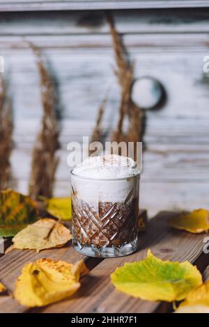 Nahaufnahme eines Glases heißen Kakaos mit Schlagsahne und Zimt, umgeben von Herbstblättern Stockfoto