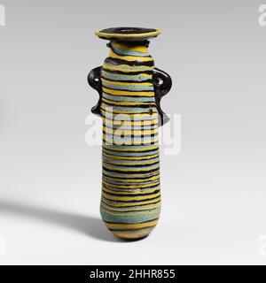 Glas-Alabastron (Parfümflasche) 5th. Jahrhundert v. Chr. Griechisch, östliches Mittelmeer blickdicht dunkelrotbraun, schwarz erscheinend, mit Griffen in gleicher Farbe; Trails in opak-gelb und türkisblau.breite horizontale Randscheibe mit abgeschrägter Kante; kurzer zylindrischer Hals, nach oben verjüngend; schmale abgerundete Schulter; gerader zylindrischer Körper, Nach oben verjüngend; konvexer Boden; zwei große vertikale Ringgriffe mit geklopften Schwänzen, über der Traildekoration angebracht; einer länger als der andere.vermengte gelbe und türkisblaue Trails am Rand der Randscheibe befestigt; eine große gelbe Trails ungleichmäßig auf den Hals aufgetragen Stockfoto
