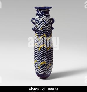 Glas-Alabastron (Parfümflasche) Ende 6th–5th Jahrhundert v. Chr. Griechisch, östliches Mittelmeer Durchscheinendes Kobaltblau, mit Griffen in gleicher Farbe; Spuren in opak-weiß und opak-gelb; leicht konkave horizontale Randscheibe, geformt als Spule, mit rauer Kante zum Mund; kein wahrnehmbarer Hals oder Schulter; Leicht konvexe Seite zum zylindrischen Körper, nach oben verjüngend; abgerundeter Boden, mit zentralem Punkt; zwei vertikale Ringgriffe mit geknallten Schwänzen, über der Traildekoration angebracht.Weißer Trail am Hals unter der Randscheibe befestigt, ungleichmäßig umwickelt, in ein unregelmäßiges Zickzackmuster eingewickelt, mit tiefem Verzug Stockfoto