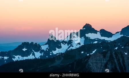 Im Sommer verblasst das Licht hinter einem Bergrücken am Mount Rainier im Bundesstaat Washington, während die zerklüfteten Felsen in den rosafarbenen Himmel reichen Stockfoto